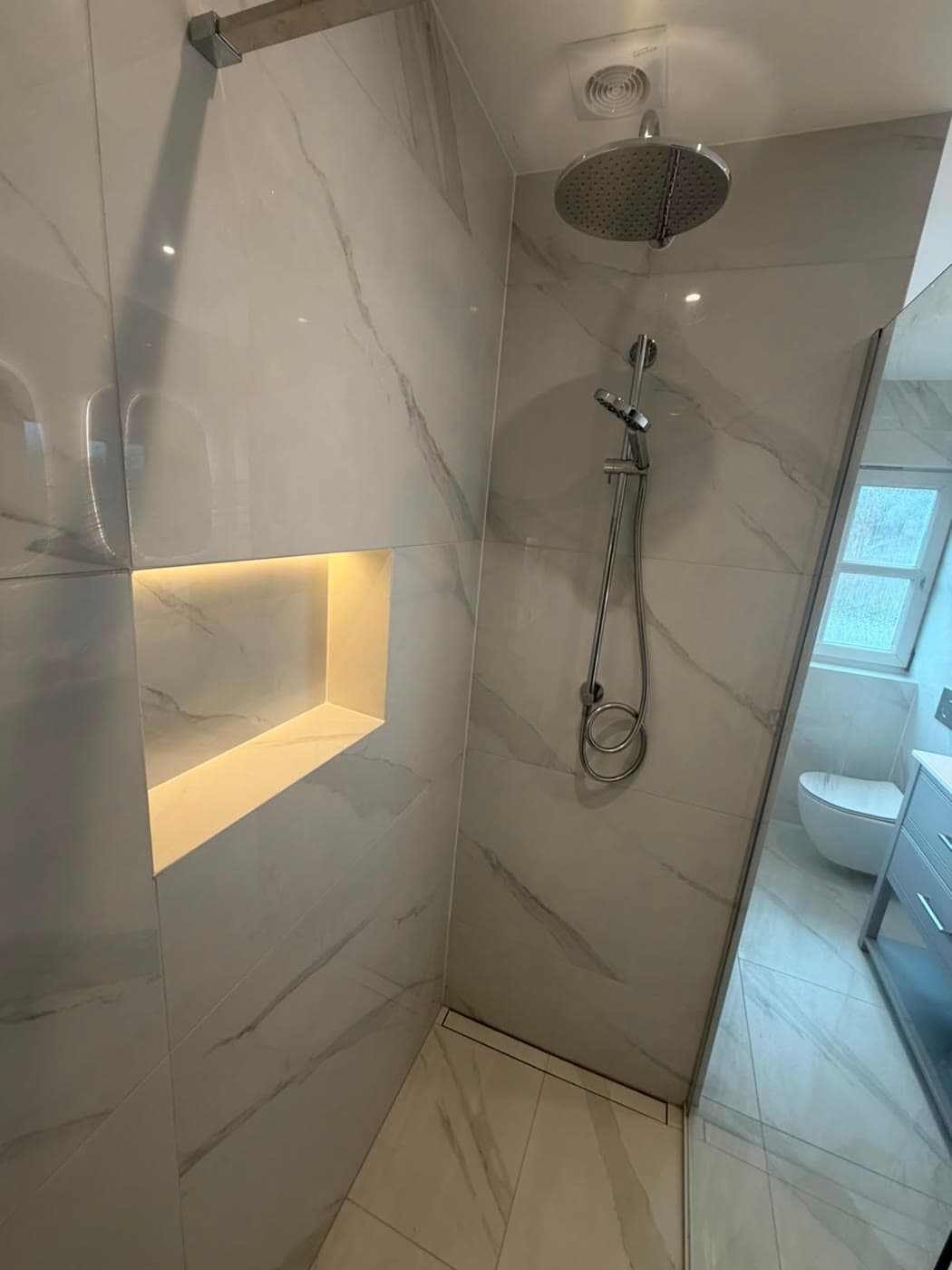 Marble tiled bathroom with a twin vanity and backlit mirrors, fitted by Caro Bathrooms
