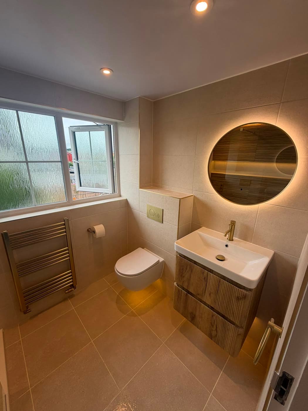 Grey tiled shower room with a wall-hung vanity and a backlit mirror, fitted by Caro Bathrooms