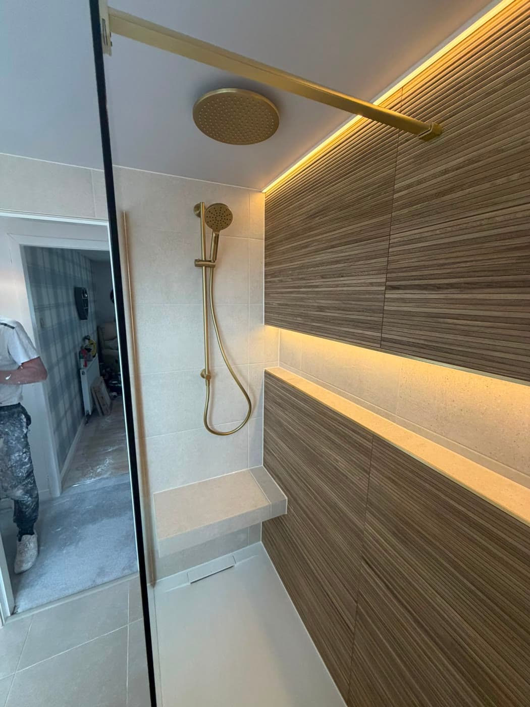 Grey tiled shower room with a wall-hung vanity and a backlit mirror, fitted by Caro Bathrooms