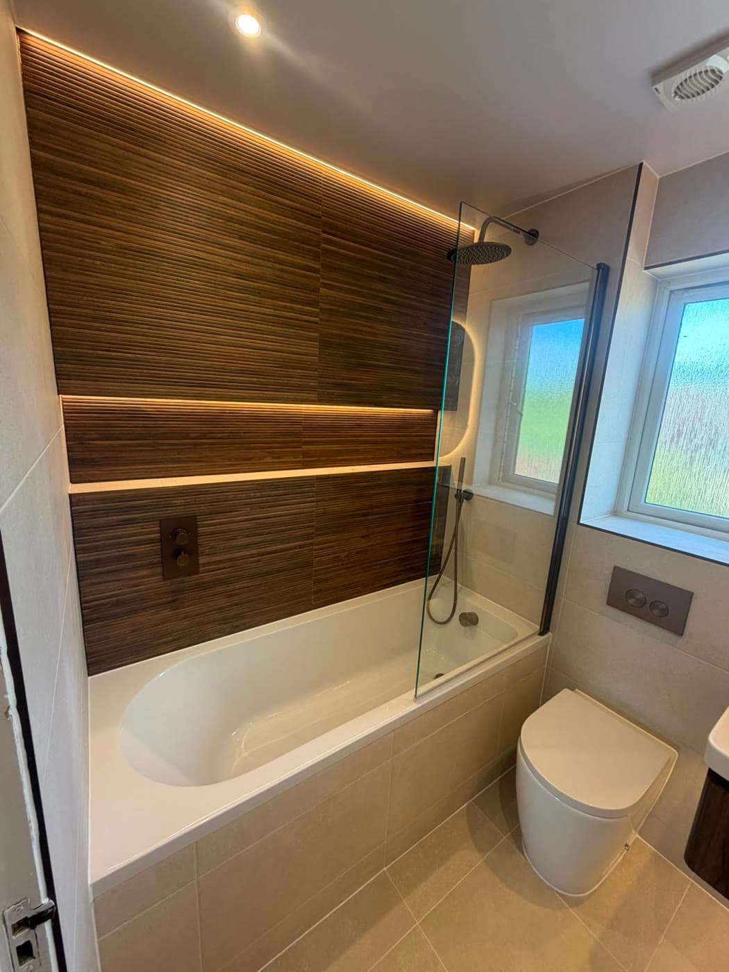Bathroom with a timber feature wall, backlit shelving and a fitted bath, fitted by Caro Bathrooms