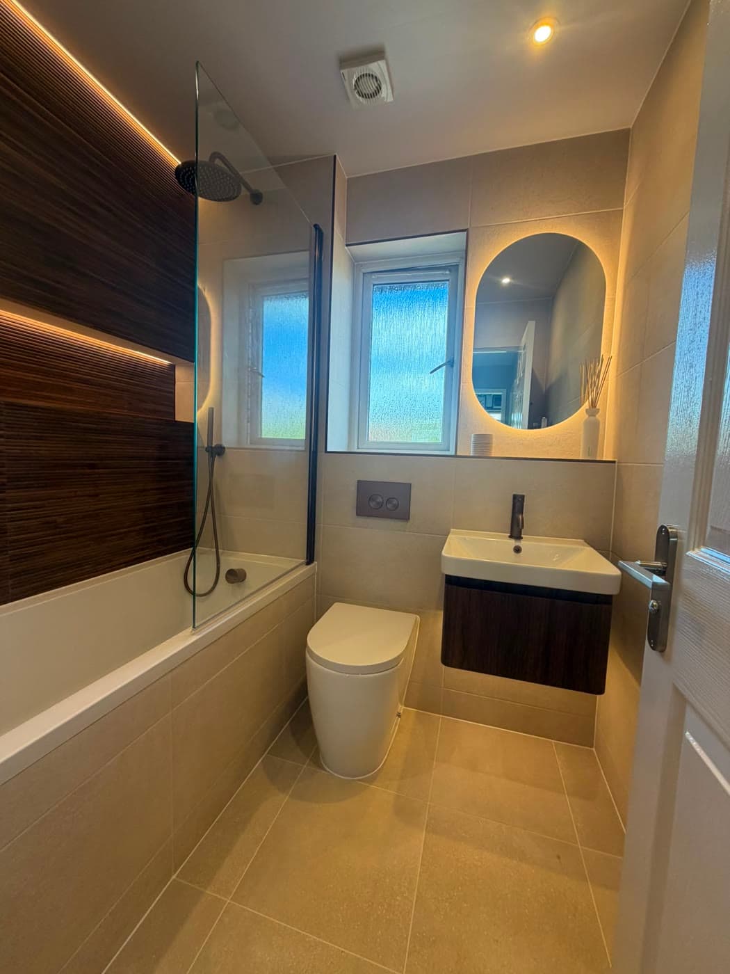 Bathroom with a timber feature wall, backlit shelving and a fitted bath, fitted by Caro Bathrooms